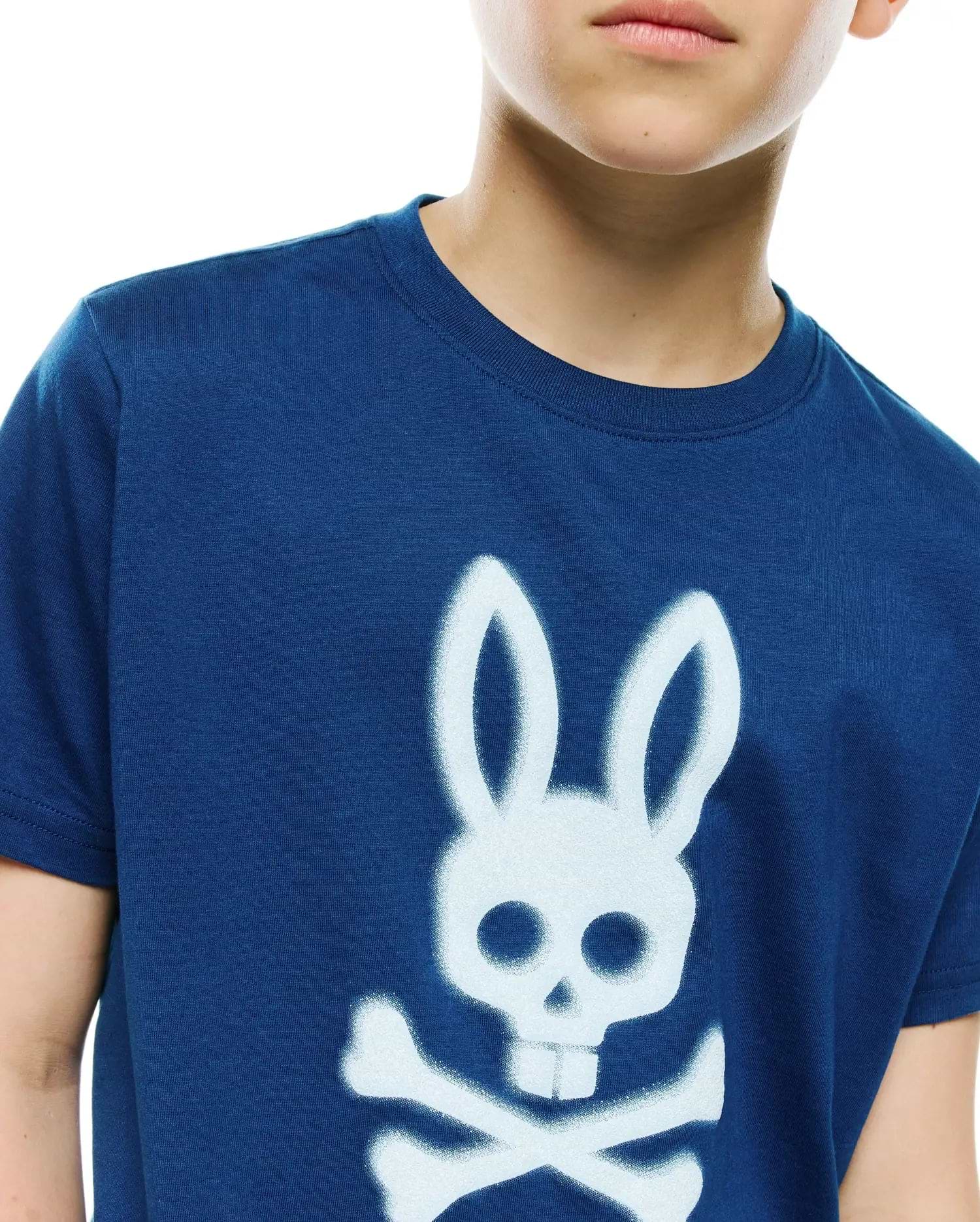 Kids Emmanuel Graphic Tee in navy blue, featuring a classic fit and soft jersey knit. A prominent, large white spray-paint effect Psycho Bunny skull and crossbones graphic adorns the central chest.