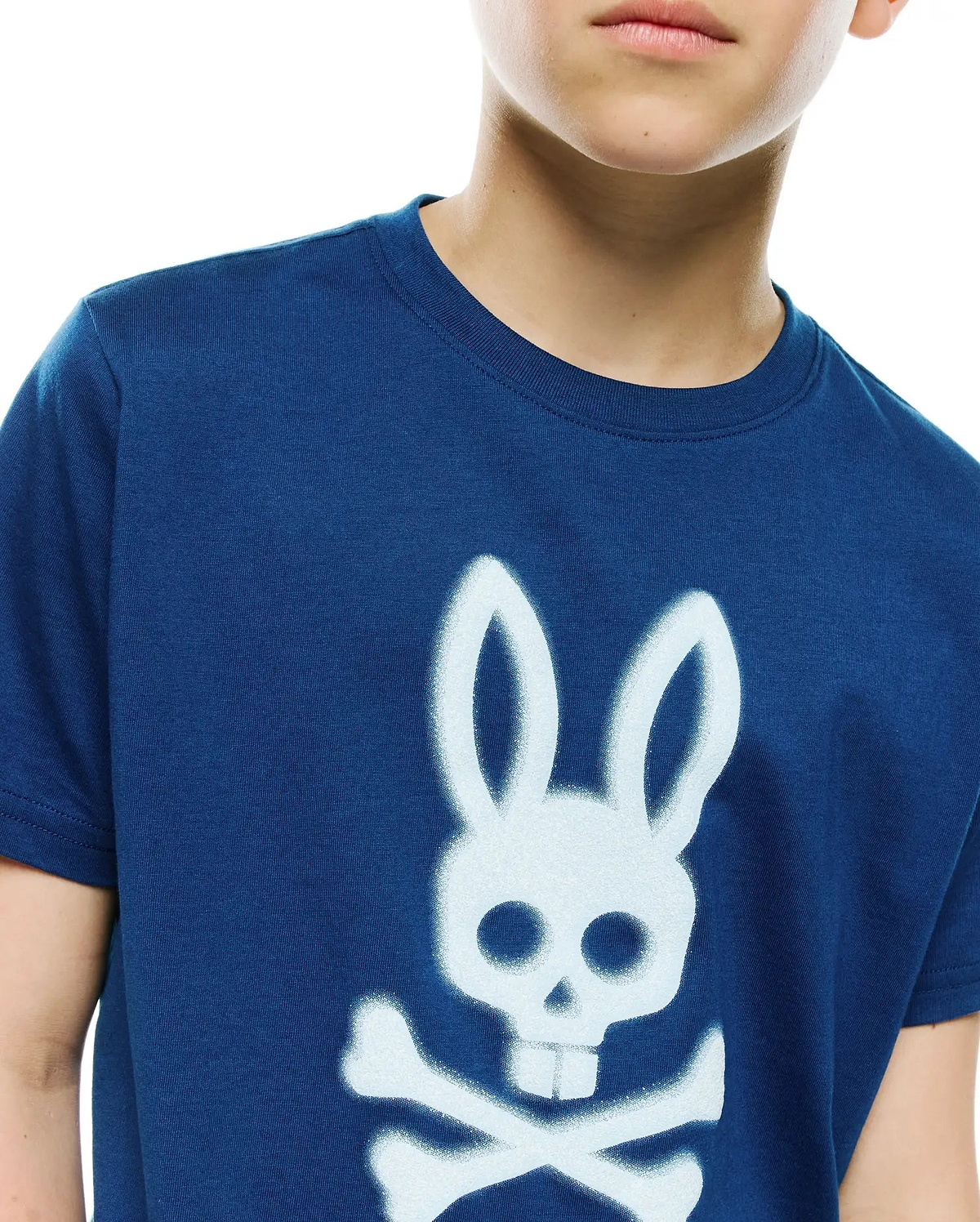 Kids Emmanuel Graphic Tee in navy blue, featuring a classic fit and soft jersey knit. A prominent, large white spray-paint effect Psycho Bunny skull and crossbones graphic adorns the central chest.