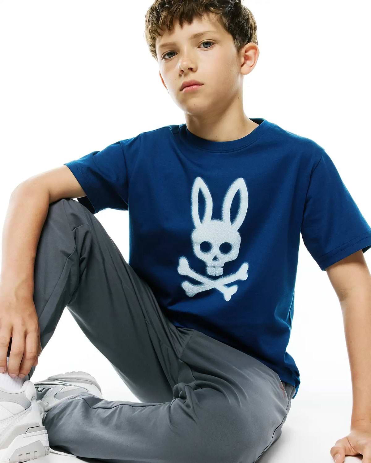 Kids Emmanuel Graphic Tee in deep blue jersey, featuring a large, distressed white Psycho Bunny skull and crossbones graphic prominently centered on the chest, in a classic fit.