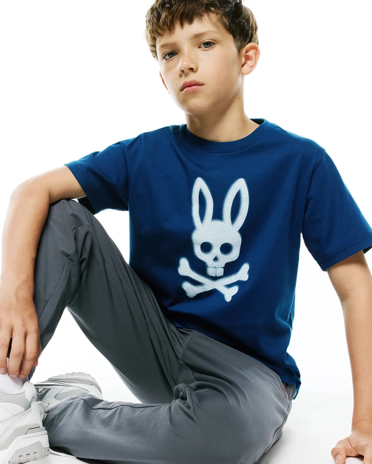 Kids Emmanuel Graphic Tee in deep blue jersey, featuring a large, distressed white Psycho Bunny skull and crossbones graphic prominently centered on the chest, in a classic fit.