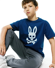 Kids Emmanuel Graphic Tee in deep blue jersey, featuring a large, distressed white Psycho Bunny skull and crossbones graphic prominently centered on the chest, in a classic fit.