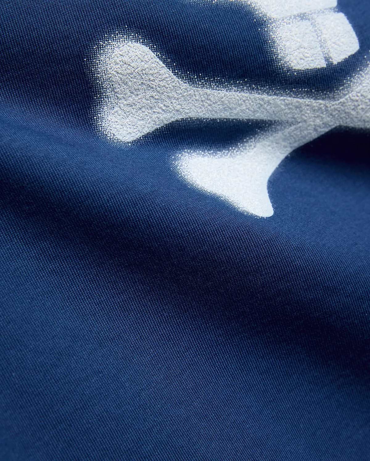 Kids Emmanuel Graphic Tee in deep navy jersey knit, featuring a large, distressed white graphic of a bone, part of the iconic Psycho Bunny skull and crossbones logo.