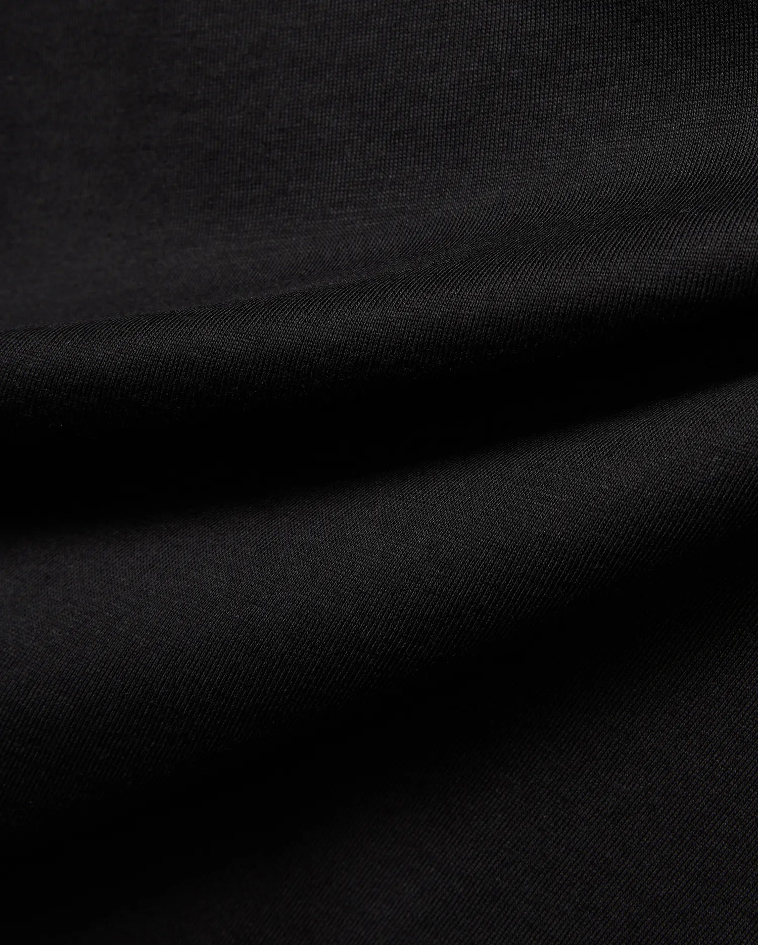 Premium black Kids Jaydon Wordmark Graphic Tee fabric, a soft, finely textured jersey knit with visible subtle ribbing and elegant draping folds, highlighting material quality.