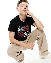 Kids Ledger Graphic Tee. Black classic fit jersey tee with a large central chest graphic featuring two Psycho Bunny skull logos, one red and one white, and Psycho Bunny text below.