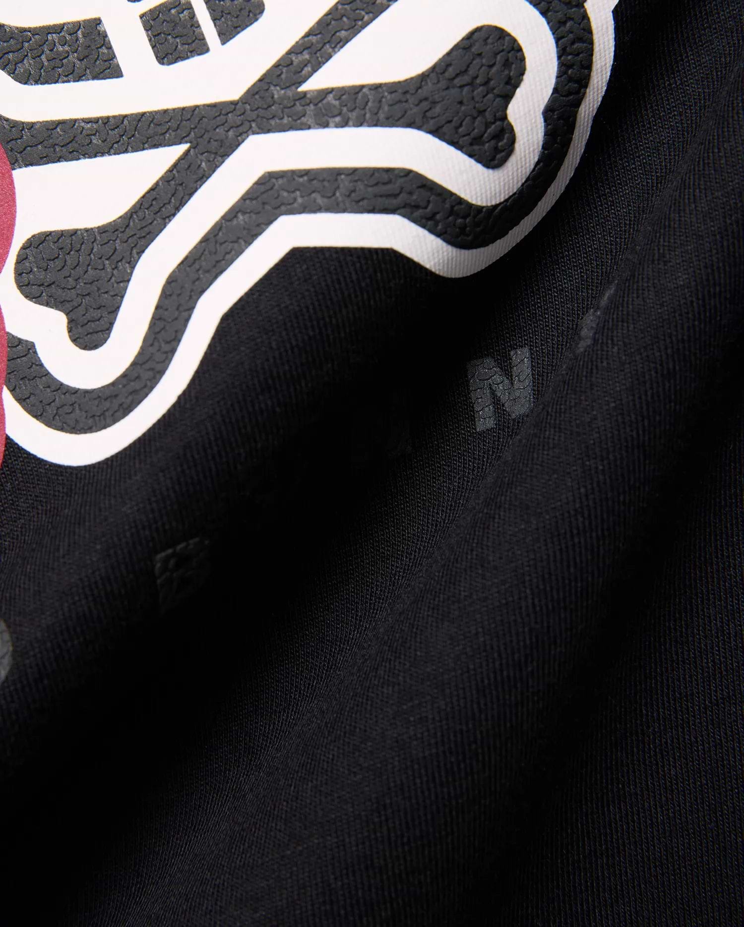 Kids Ledger Graphic Tee in black jersey knit, featuring a large, raised white and textured black Psycho Bunny skull graphic with a hint of dark pink, and subtle background letter prints.