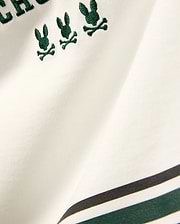 Kids Mike Graphic Jersey Tee in white jersey knit, featuring multiple small embroidered dark green Psycho Bunny skull logos and a bottom stripe design with dark green and black accents.