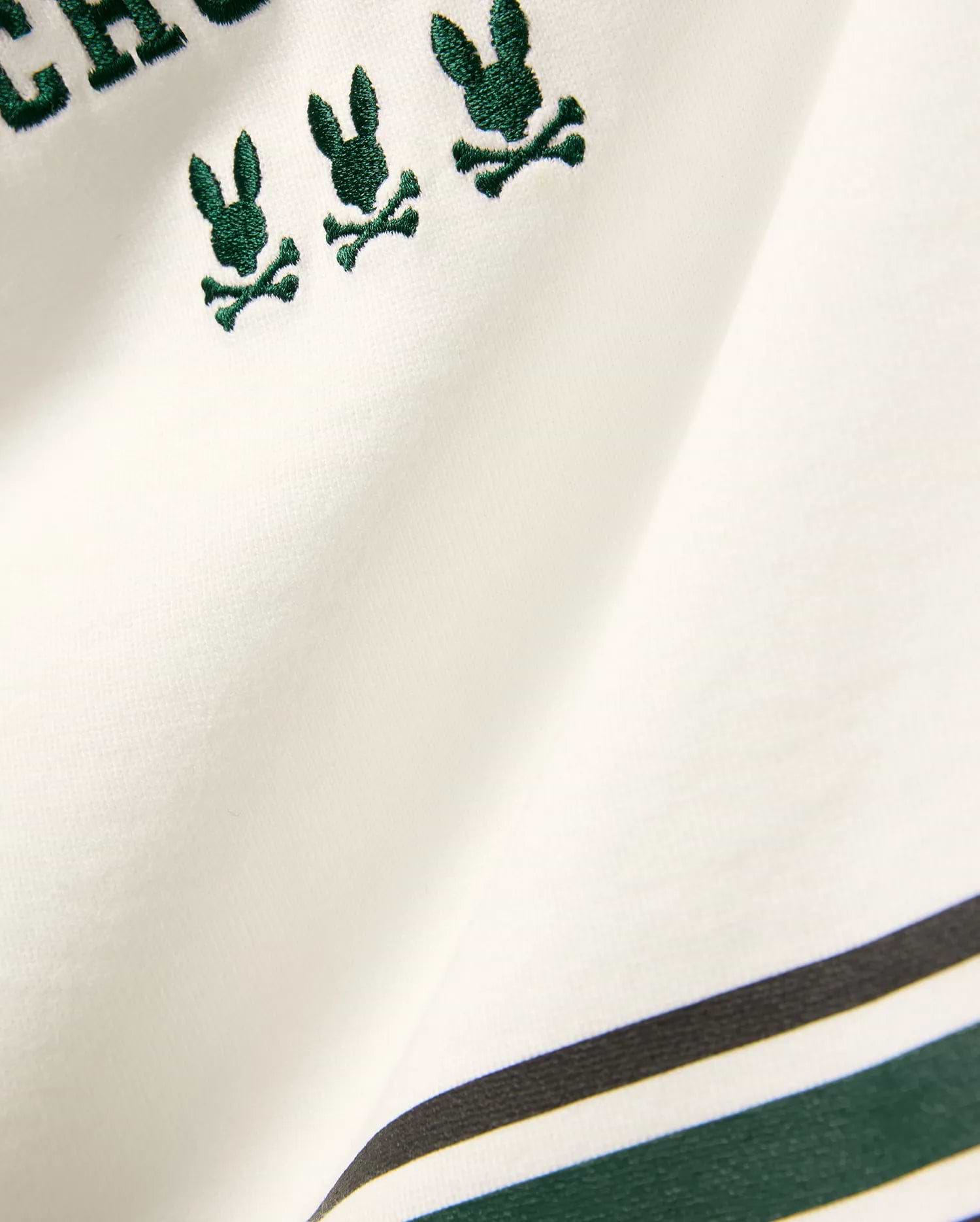 Kids Mike Graphic Jersey Tee in white jersey knit, featuring multiple small embroidered dark green Psycho Bunny skull logos and a bottom stripe design with dark green and black accents.