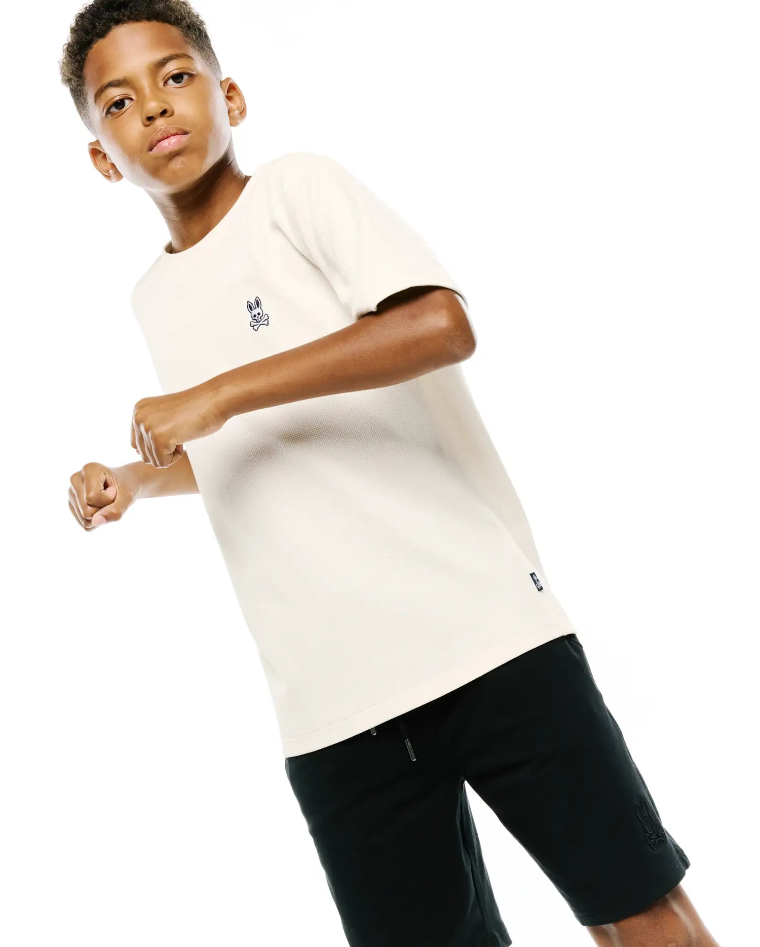 Kids Maxton Waffle Tee, a cream classic fit waffle knit t-shirt featuring a small embroidered dark blue Psycho Bunny skull logo on the left chest and a woven brand tag on the hem.