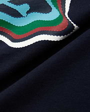 Kids' Klaus Graphic Tee in navy jersey knit, featuring a large, textured graphic print with wavy lines in blue, green, red, and white, hinting at the iconic Psycho Bunny skull. (6)