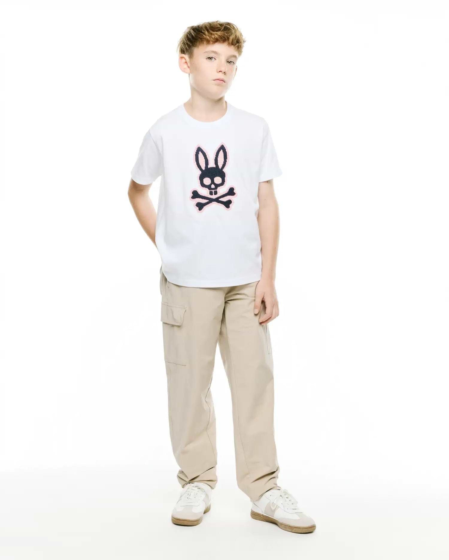 Kids' Samson Pima Graphic Tee, a white classic fit jersey t-shirt featuring a large black and pink Psycho Bunny skull and crossbones graphic print on the center chest, paired with relaxed fit khaki cargo pants. (5)