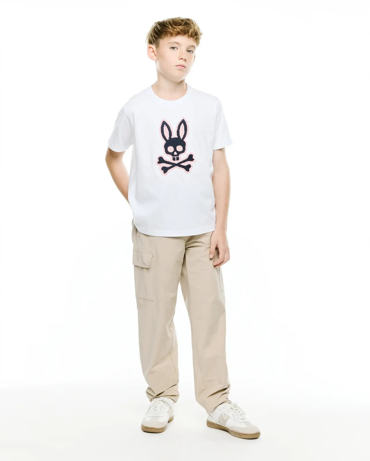 Kids' Samson Pima Graphic Tee, a white classic fit jersey t-shirt featuring a large black and pink Psycho Bunny skull and crossbones graphic print on the center chest, paired with relaxed fit khaki cargo pants. (5)
