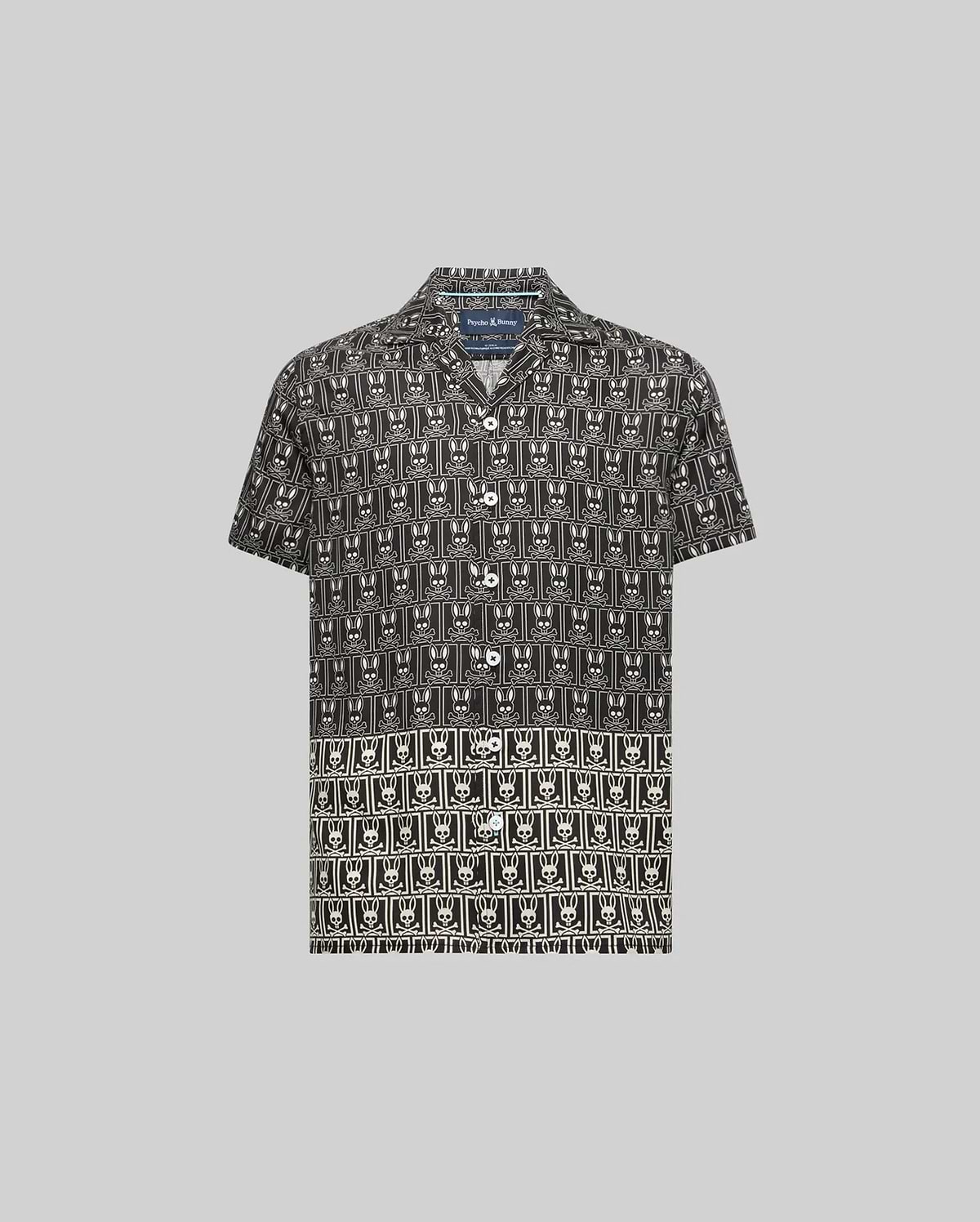 Kids Keon Tencel Shirt, a black short-sleeve camp collar shirt featuring a relaxed fit and an all-over white repeating Psycho Bunny skull and crossbones logo pattern.