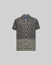 Kids Keon Tencel Shirt, a black short-sleeve camp collar shirt featuring a relaxed fit and an all-over white repeating Psycho Bunny skull and crossbones logo pattern.