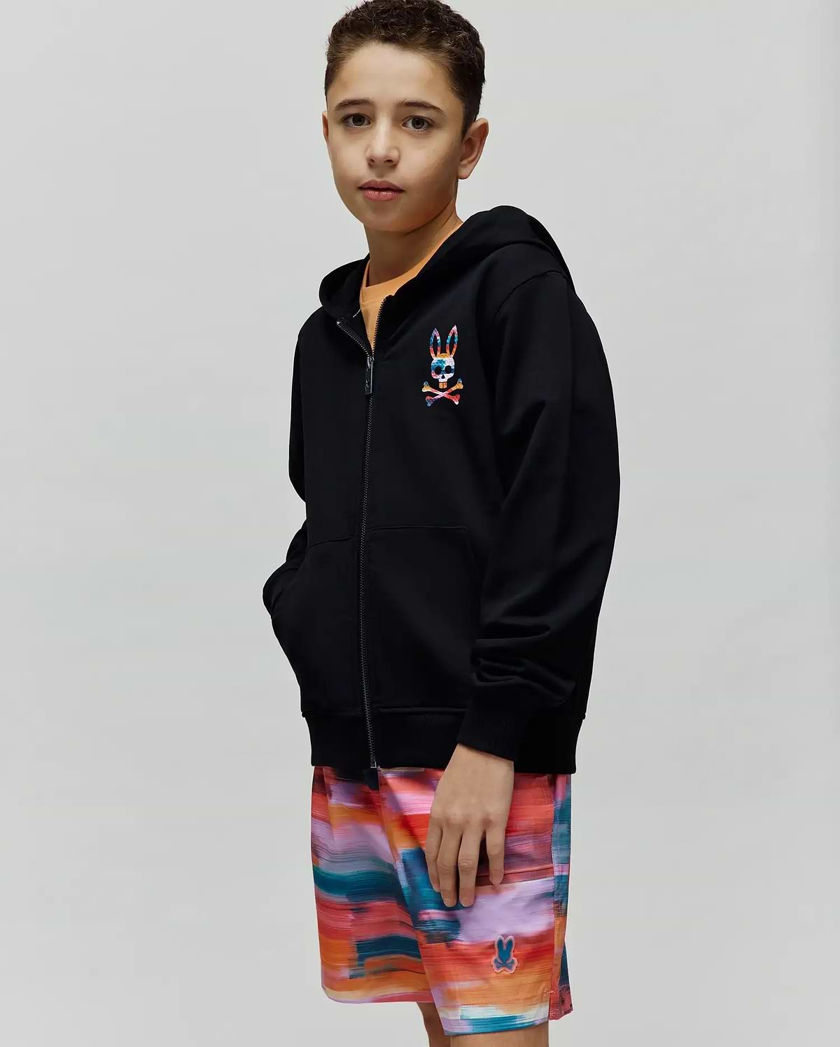Kids Raphael French Terry Full Zip Hoodie in black, featuring a relaxed fit and a small, embroidered, multi-colored Psycho Bunny skull and crossbones logo on the left chest.