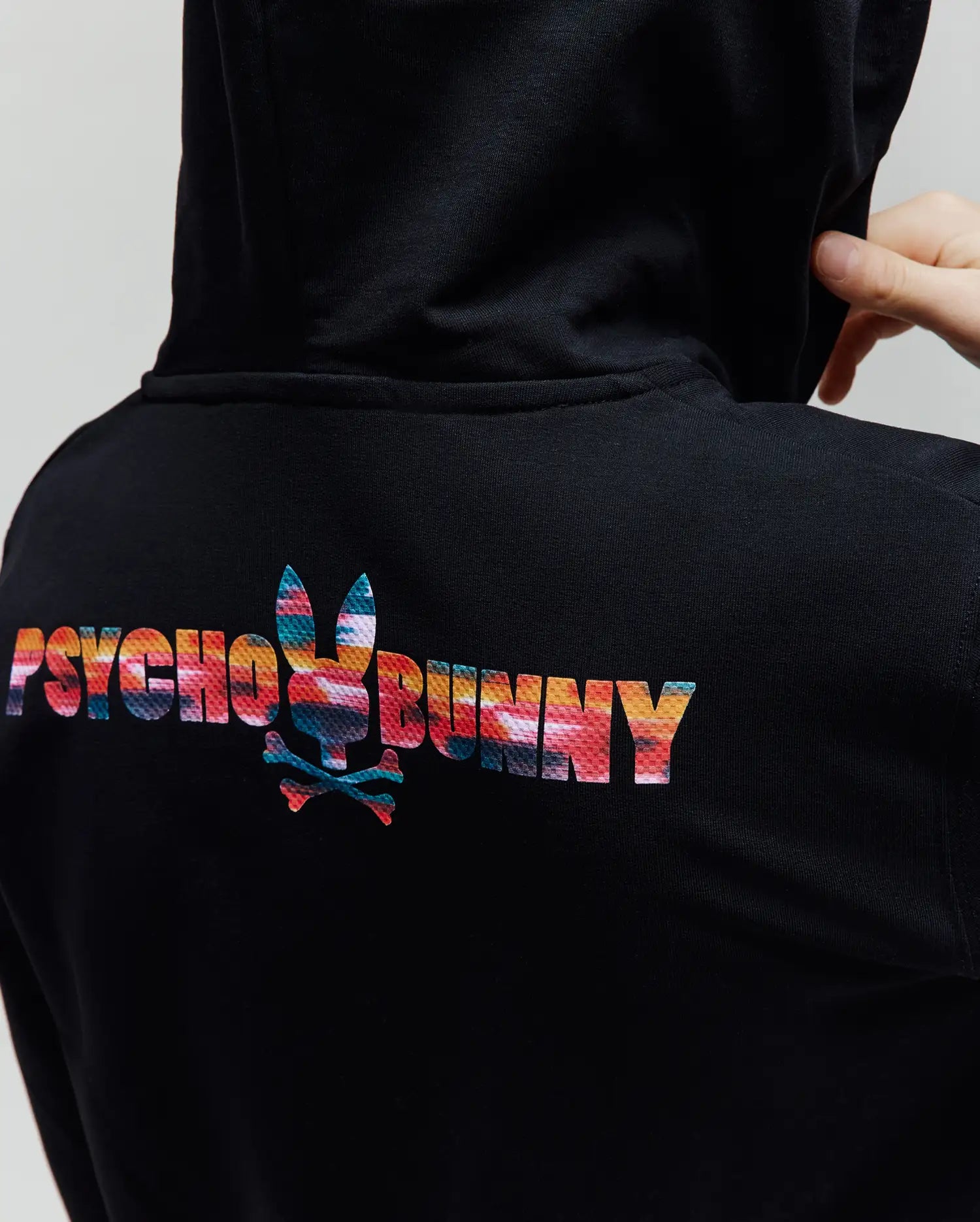 Kids Raphael French Terry Full Zip Hoodie in black, featuring a large, vibrant abstract multicolor Psycho Bunny text and bunny skull logo on the upper back, with a classic fit.