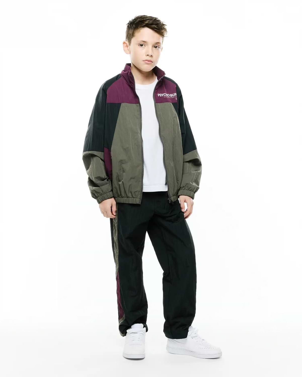Kids Alder Nylon Colorblock Jacket in black, olive green, and deep plum, featuring a relaxed fit, full zip, and small white Psycho Bunny text logo on the left chest, paired with matching track pants.