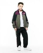 Kids Alder Nylon Colorblock Jacket in black, olive green, and deep plum, featuring a relaxed fit, full zip, and small white Psycho Bunny text logo on the left chest, paired with matching track pants.