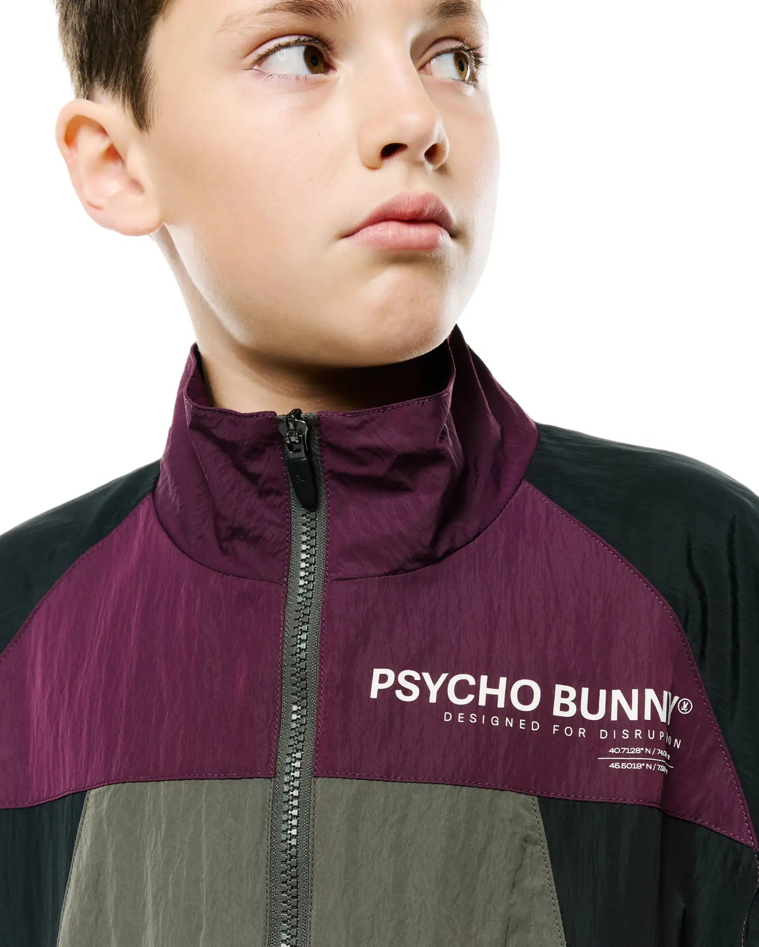 Kids Alder Nylon Colorblock Jacket featuring a plum, dark green, and olive green crinkled nylon fabric, full-zip front, high collar, and a large white Psycho Bunny logo with Designed For Disruption text on the chest.