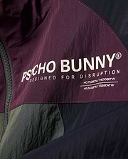 Kids Alder Nylon Colorblock Jacket in plum, olive, and navy, featuring a large white Psycho Bunny logo, Designed For Disruption text, and coordinates on crinkled nylon fabric.