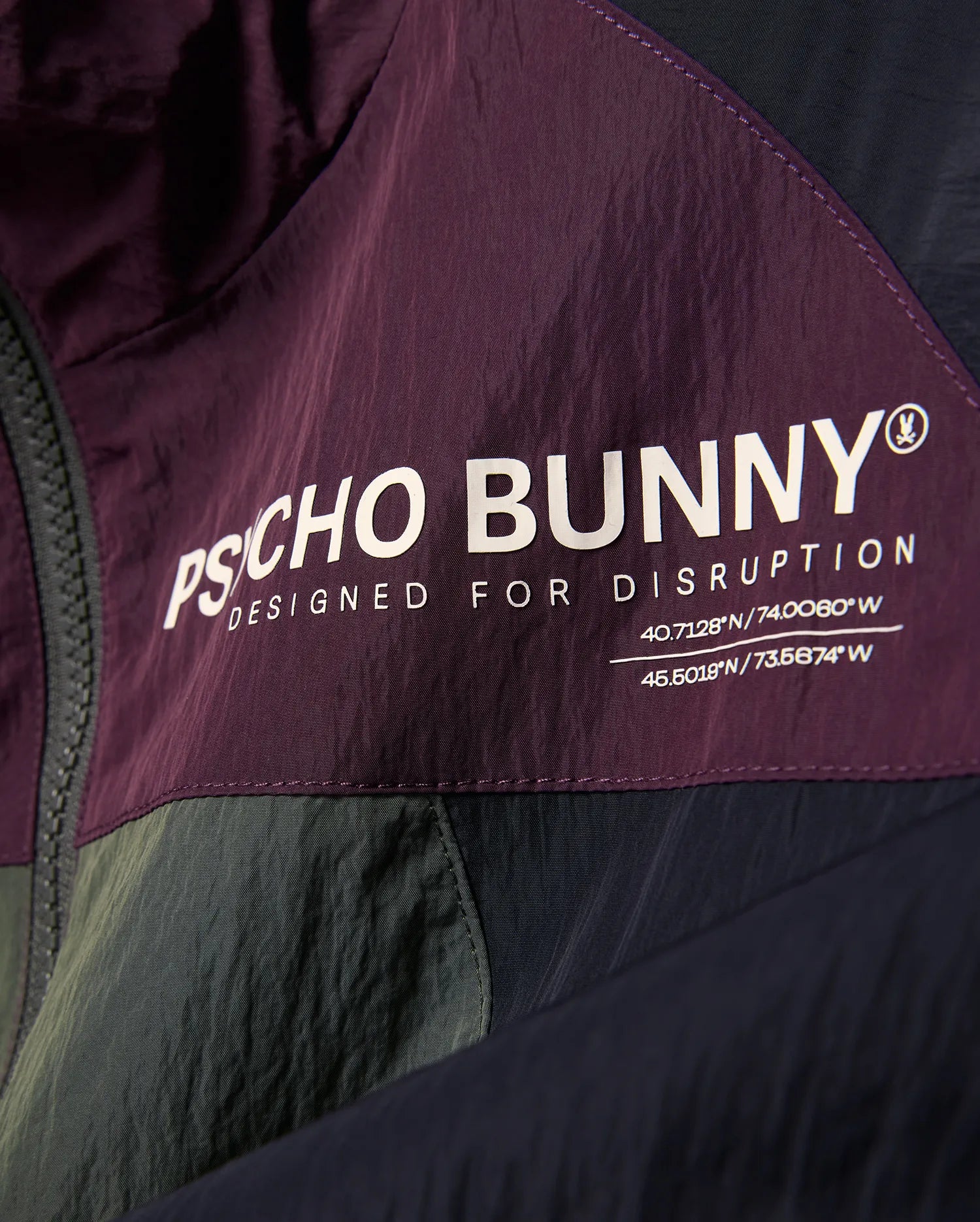 Kids Alder Nylon Colorblock Jacket in plum, olive, and navy, featuring a large white Psycho Bunny logo, Designed For Disruption text, and coordinates on crinkled nylon fabric.