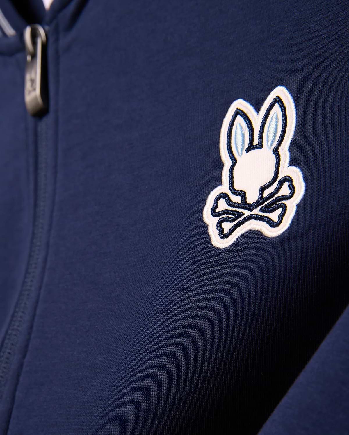 Kids Jaydon Track Jacket in navy blue, featuring a smooth knit fabric and a prominent embroidered white and light blue Psycho Bunny skull logo on the left chest, with a metallic zipper pull.