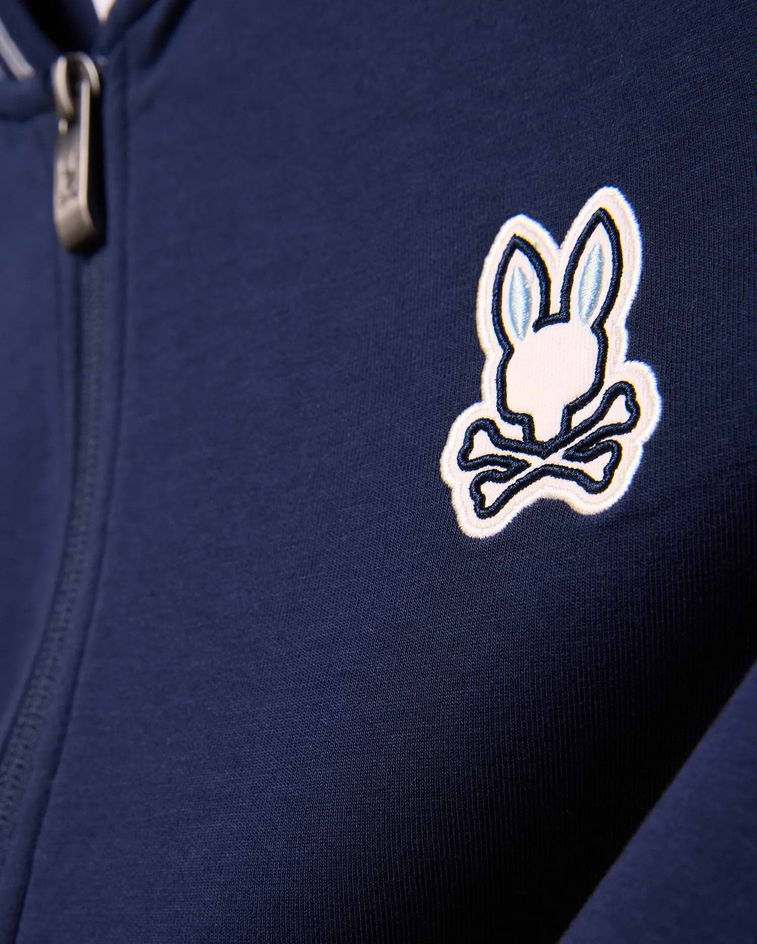 Kids Jaydon Track Jacket in navy blue, featuring a smooth knit fabric and a prominent embroidered white and light blue Psycho Bunny skull logo on the left chest, with a metallic zipper pull.