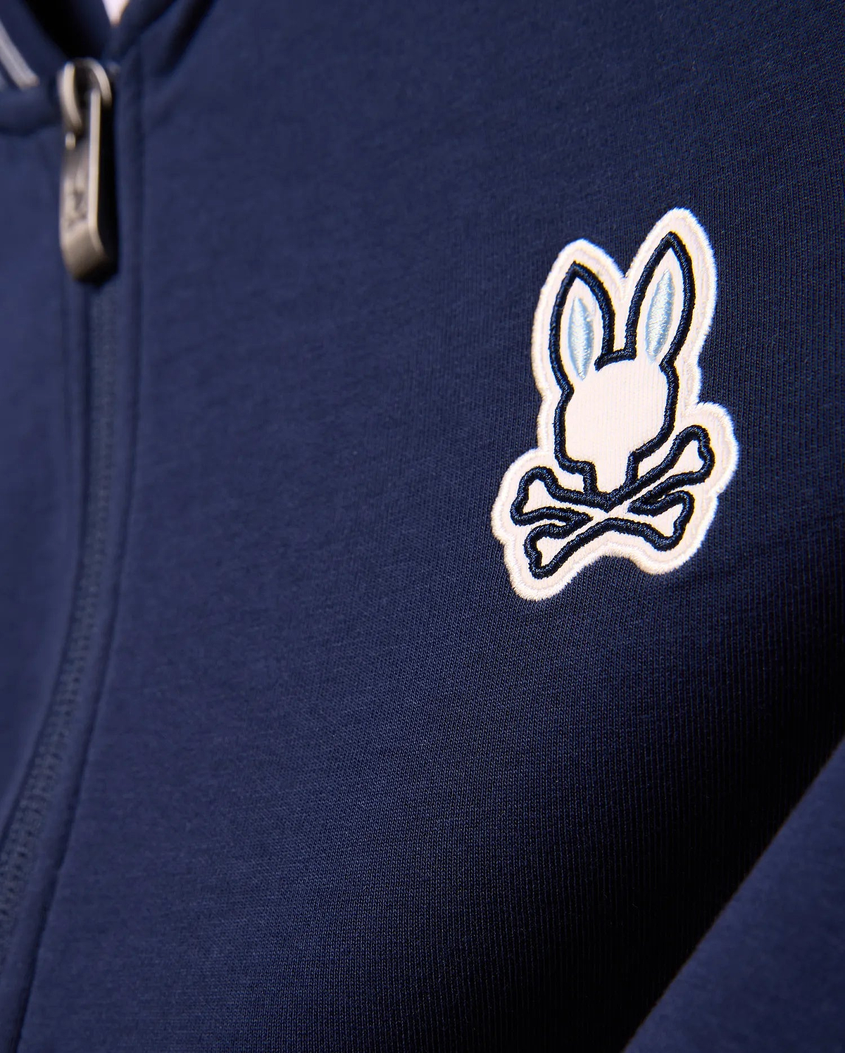 Kids Jaydon Track Jacket in navy blue, featuring a smooth knit fabric and a prominent embroidered white and light blue Psycho Bunny skull logo on the left chest, with a metallic zipper pull.