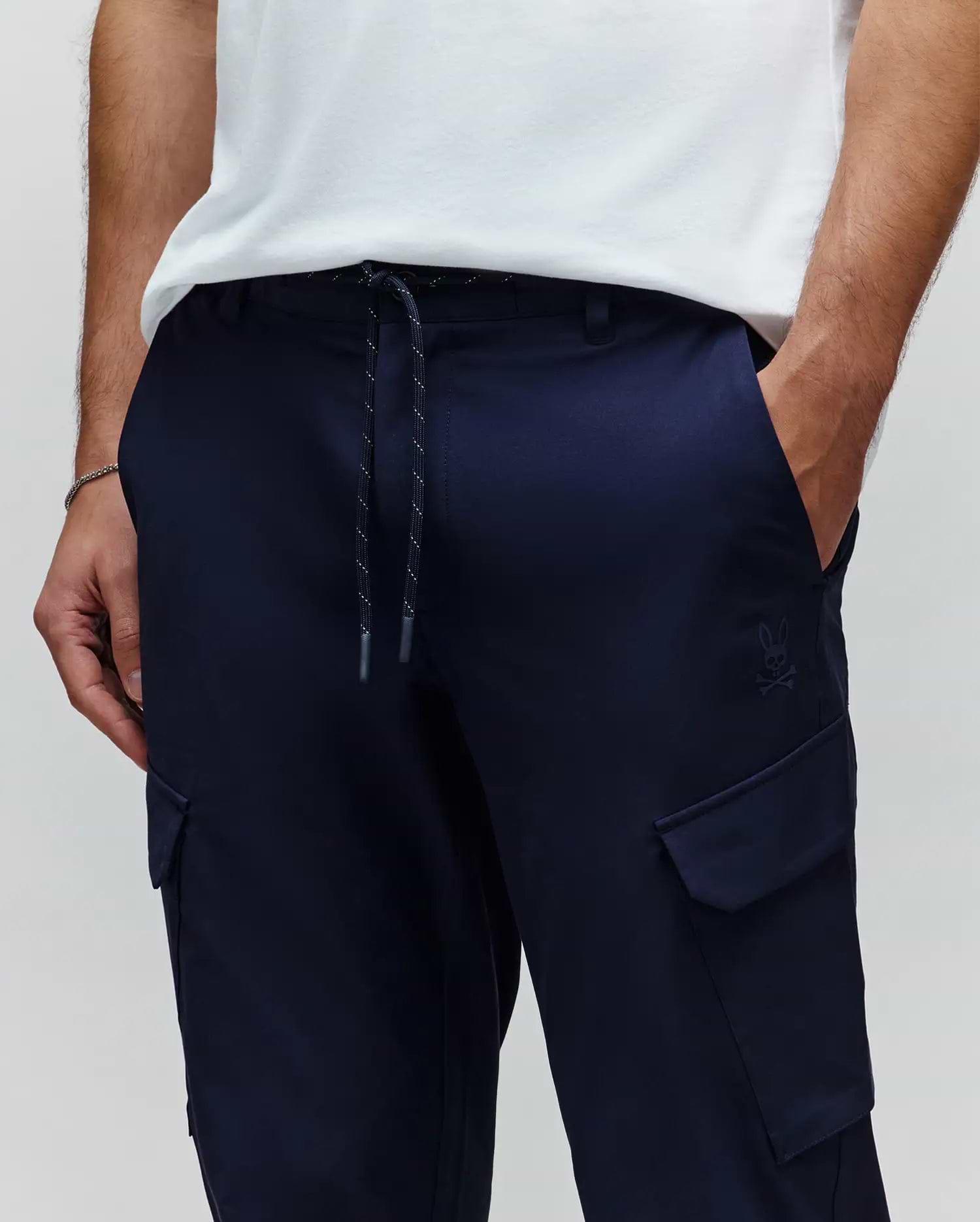 MENS LUKA CARGO PANT in navy blue, featuring a relaxed fit, smooth fabric, drawstring waist with white flecks, side cargo pockets, and a small tonal embroidered Psycho Bunny skull logo. (2)