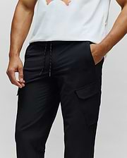 Mens Luka Cargo Pant, black, relaxed fit with smooth fabric, featuring a drawstring waist with orange flecks and a small tonal embroidered Psycho Bunny skull logo on the right cargo pocket.
