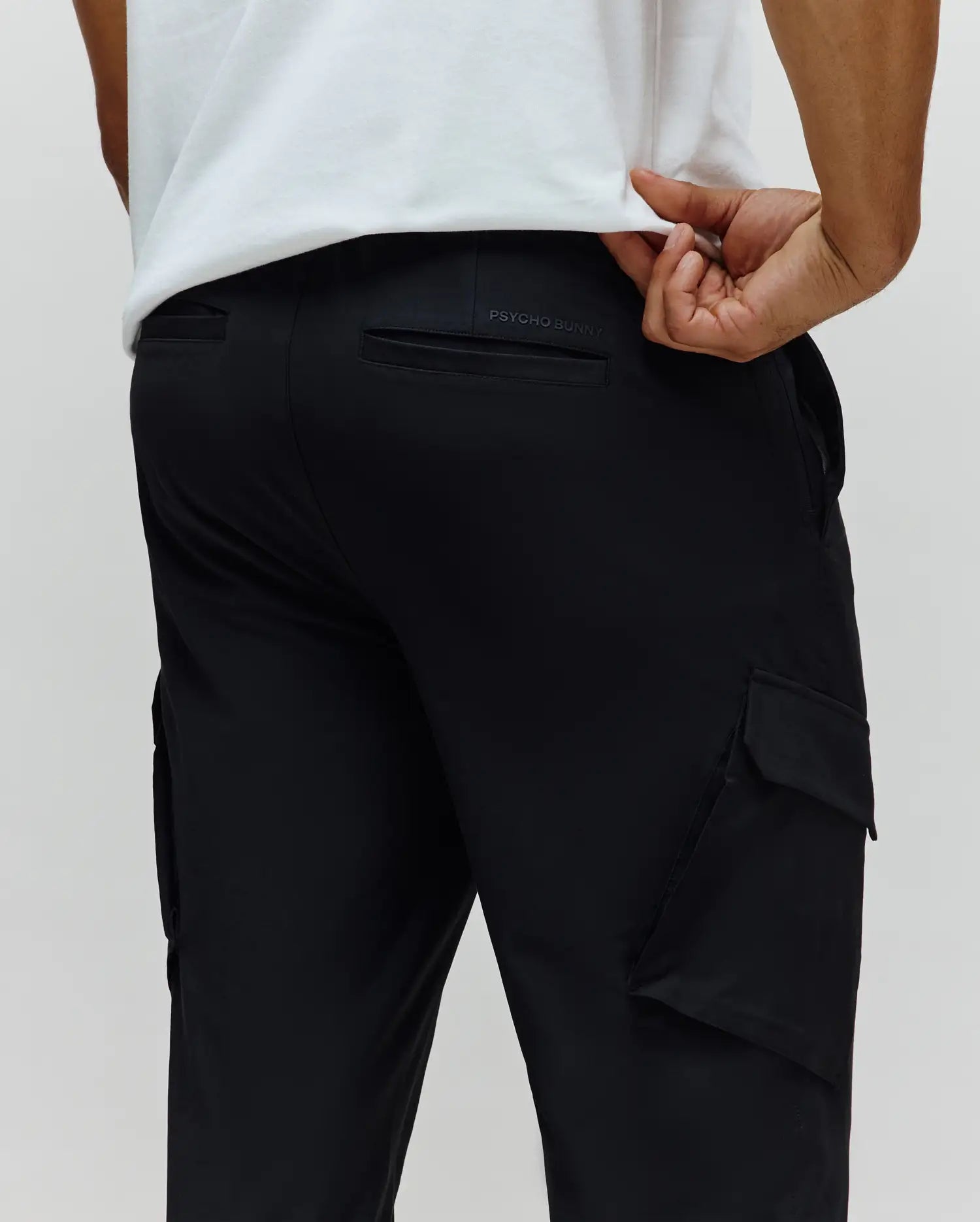 Black Mens Luka Cargo Pant in a relaxed fit, featuring a smooth, durable fabric, practical side cargo pockets, and subtle embossed PSYCHO BUNNY branding on the back waistband.