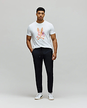 White classic fit jersey t-shirt with a large, colorful watercolor Psycho Bunny skull logo on the chest, paired with black slim fit Mens Luka Cargo Pant featuring a drawstring waist and side pockets.
