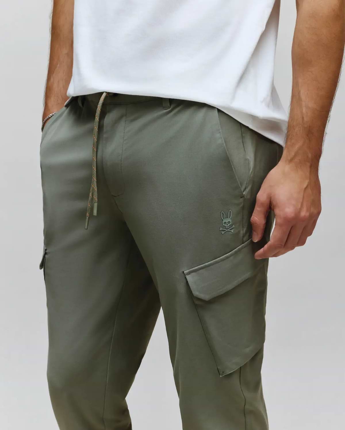 Mens Luka Cargo Pant in olive green, featuring a relaxed fit, smooth fabric, drawstring waist with speckled cord, and a small tonal embroidered Psycho Bunny skull logo above the left cargo pocket.