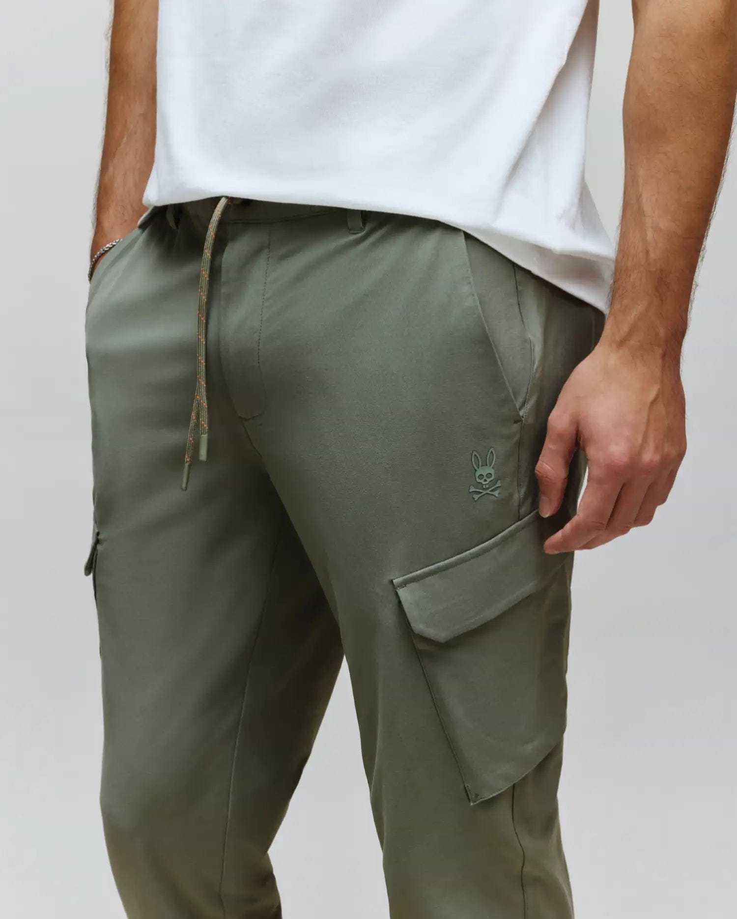 Mens Luka Cargo Pant in olive green, featuring a relaxed fit, smooth fabric, drawstring waist with speckled cord, and a small tonal embroidered Psycho Bunny skull logo above the left cargo pocket.