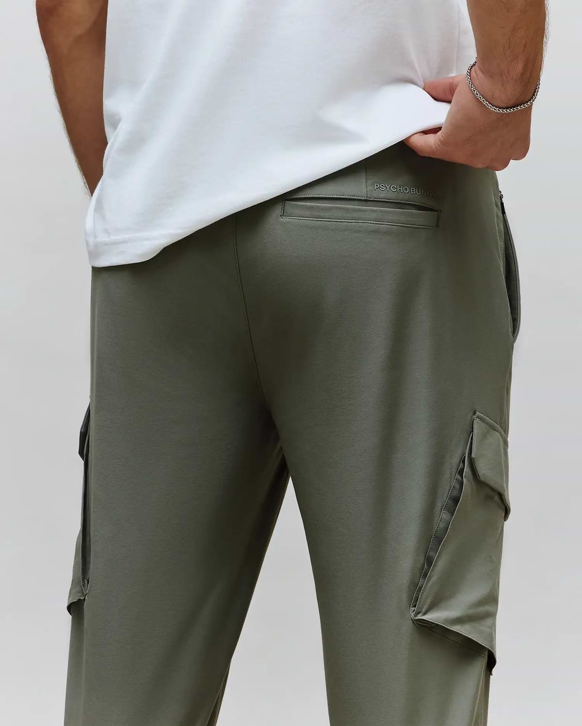 Mens Luka Cargo Pant in olive green, a relaxed fit style crafted from smooth jersey fabric, featuring prominent side cargo pockets and a debossed Psycho Bunny text logo above the back pocket.
