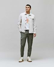 Mens Luka Cargo Pant in olive green, a white jersey t-shirt with a vibrant Psycho Bunny skull graphic, and a light beige classic fit overshirt with chest pockets.
