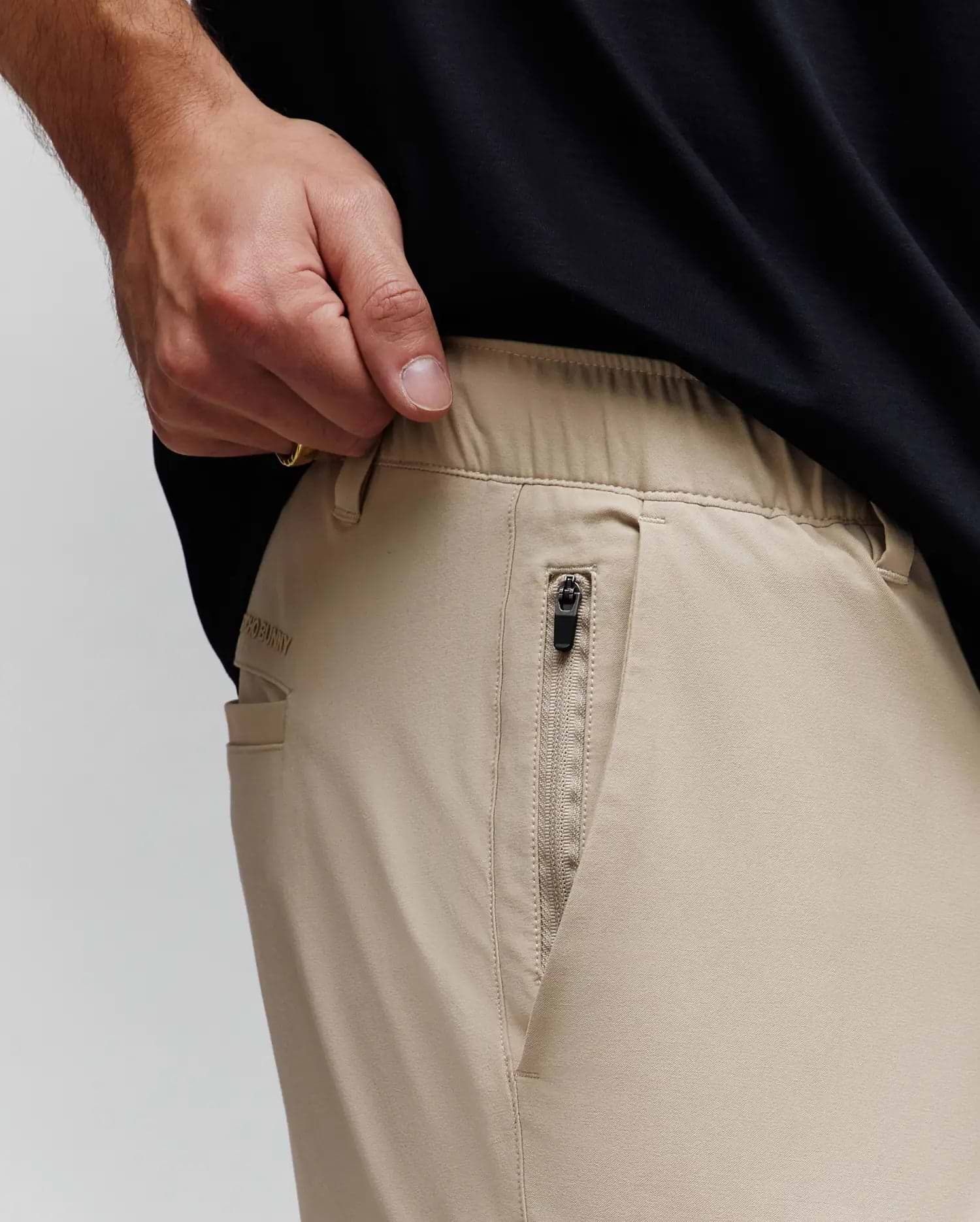 Mens Luka Cargo Pant, khaki, relaxed fit, smooth fabric, elasticated waistband, zippered side pocket with black pull, subtle embroidered Psycho Bunny text on back pocket.