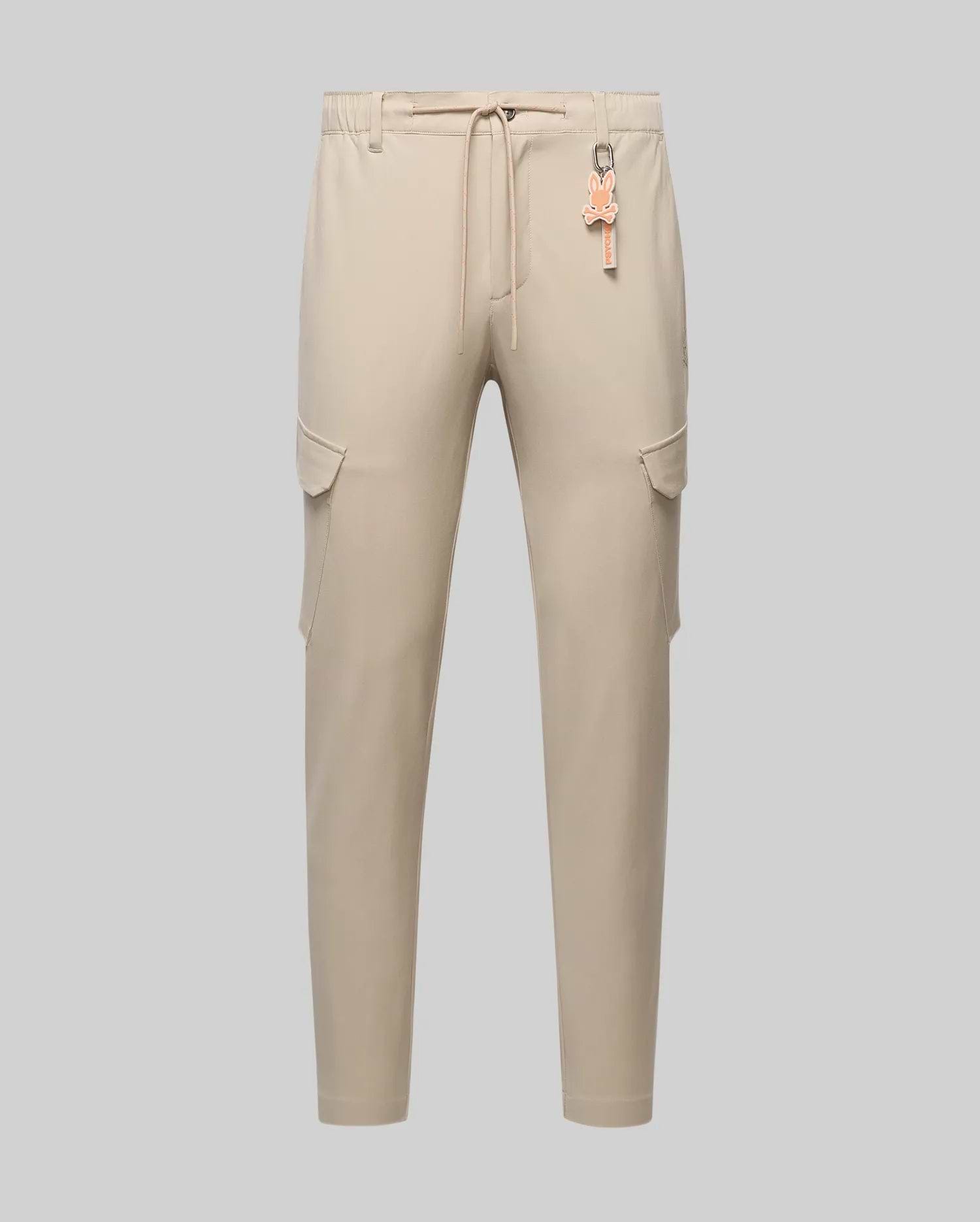 Light beige Mens Luka Cargo Pant with a relaxed fit, smooth fabric, elastic drawstring waist, side flap cargo pockets, and a vibrant orange Psycho Bunny skull logo keychain.