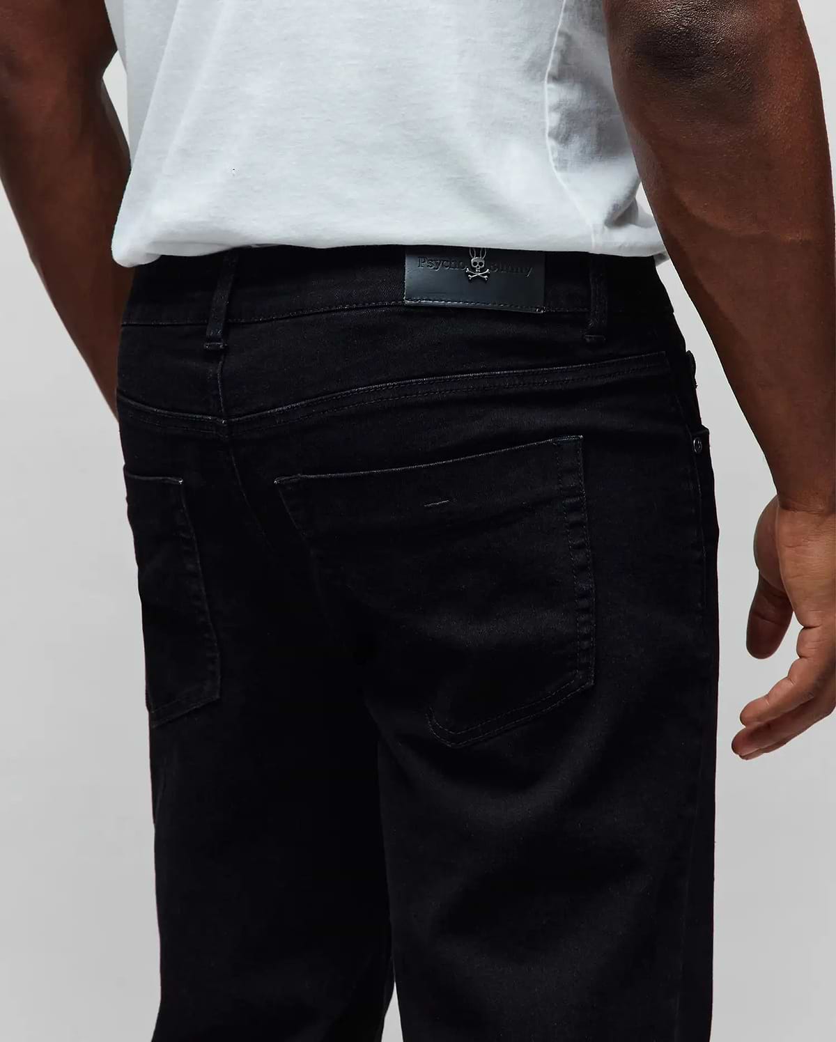 Black Mens Emerson Denim Pant, classic fit, with a black leather Psycho Bunny logo patch featuring a metallic skull on the back waistband, made from premium denim.