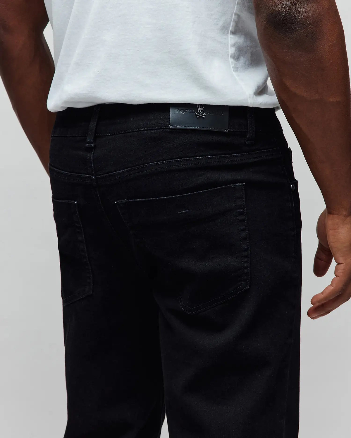 Black Mens Emerson Denim Pant, classic fit, with a black leather Psycho Bunny logo patch featuring a metallic skull on the back waistband, made from premium denim.
