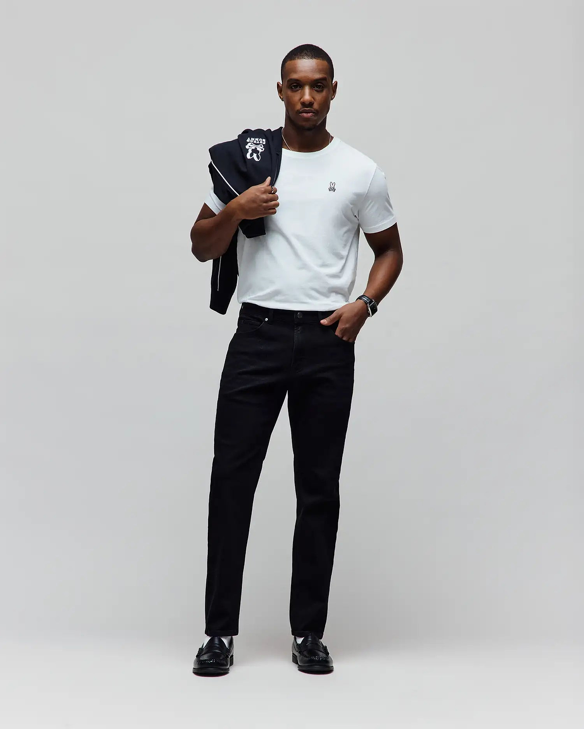 Classic fit white jersey t-shirt with small embroidered Psycho Bunny logo, black track jacket with large white logo and piping, and black Mens Emerson Denim Pant.