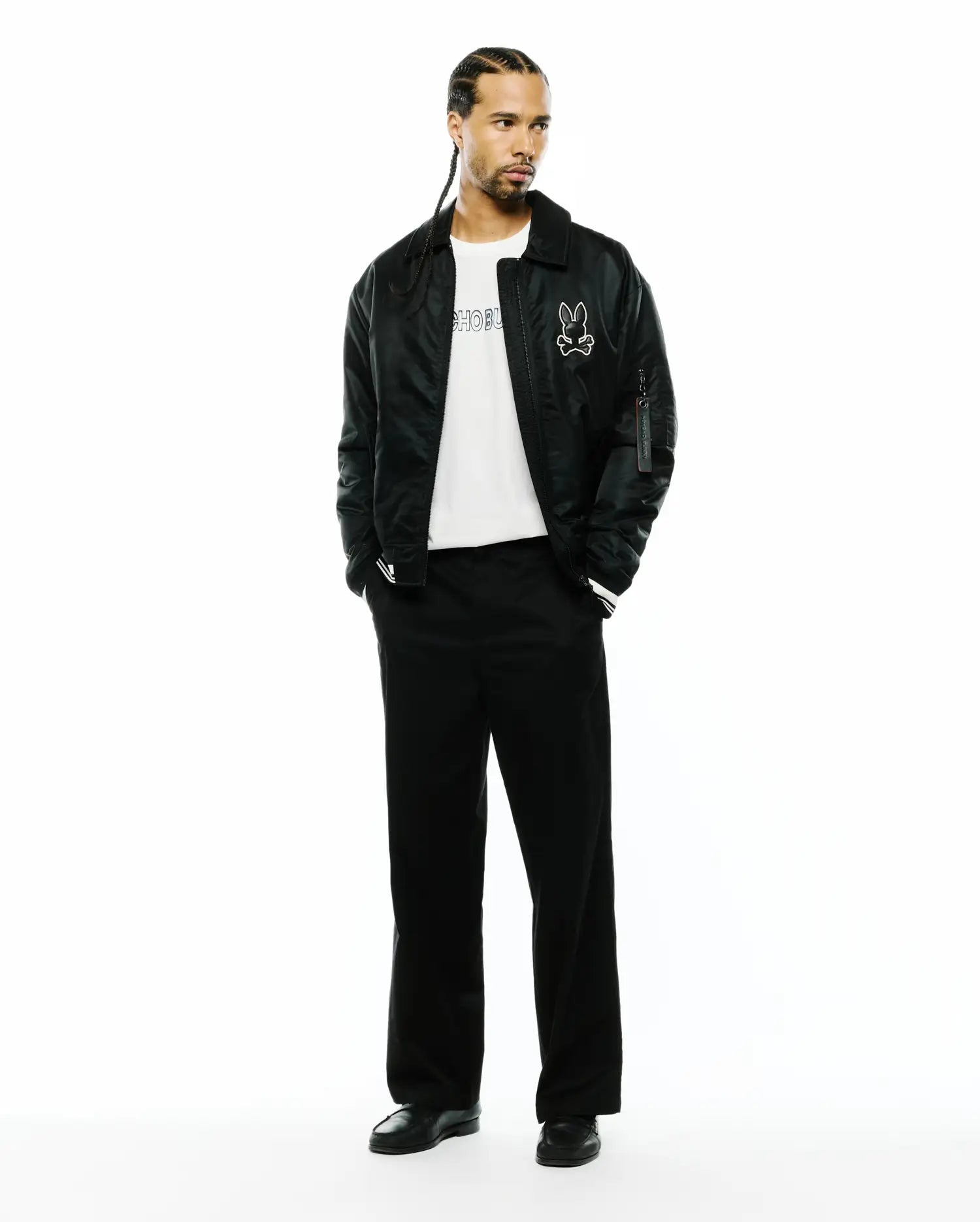 Black satin-like bomber jacket with a large white Psycho Bunny skull logo, a white jersey t-shirt with black Psycho Bunny text, and relaxed fit Black Mens Aidan Chino Pant. (4)