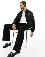 Black bomber jacket with white striped cuffs and embroidered Psycho Bunny skull logo, white jersey t-shirt with black Psycho Bunny text, and black Mens Aidan Chino Pant. (1)