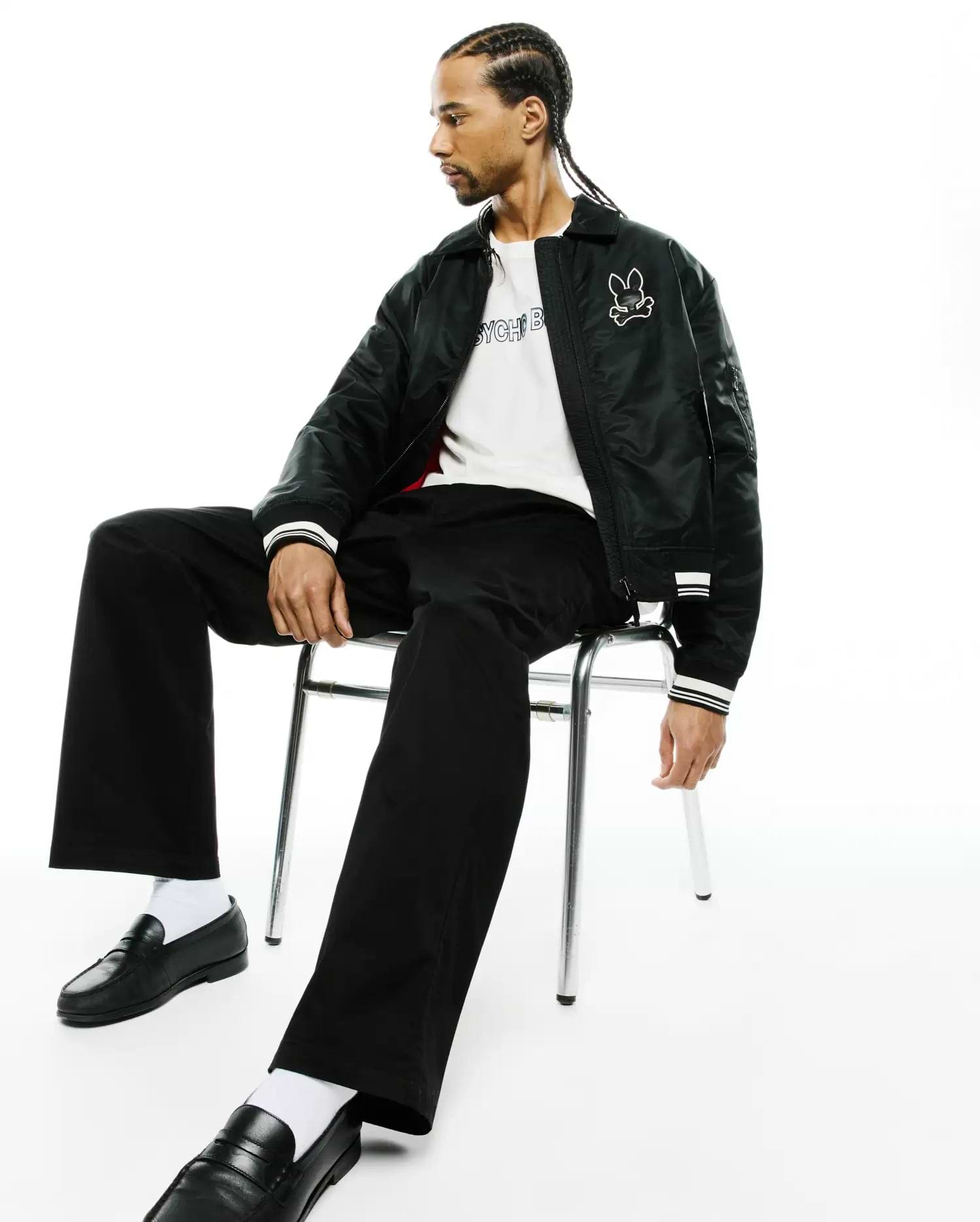 Black bomber jacket with white striped cuffs and embroidered Psycho Bunny skull logo, white jersey t-shirt with black Psycho Bunny text, and black Mens Aidan Chino Pant. (1)