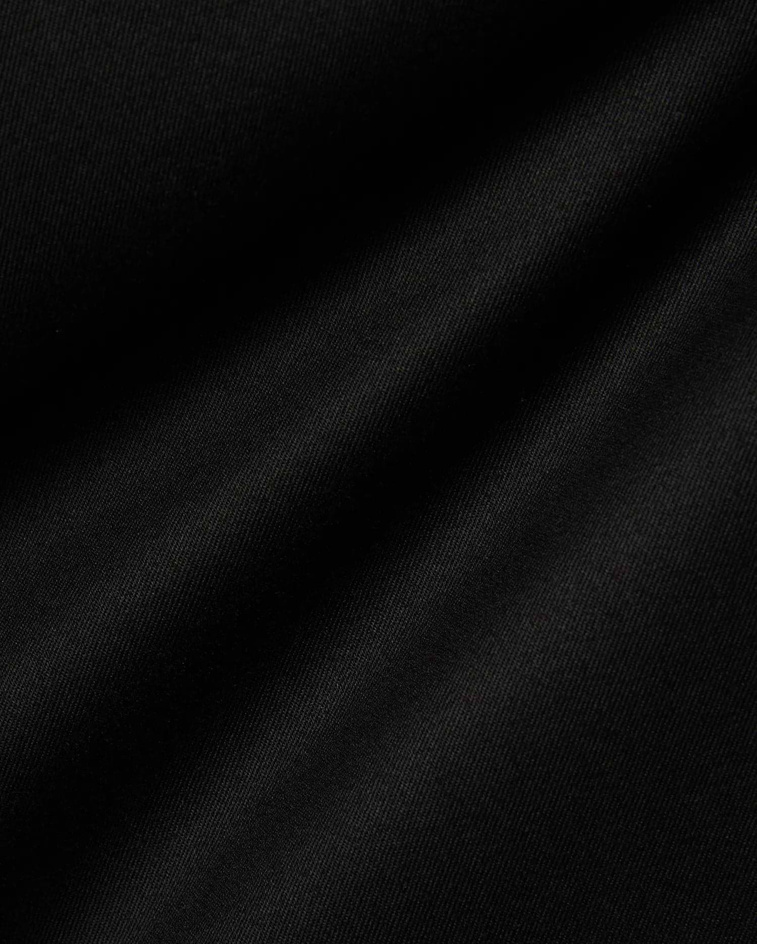 Mens Aidan Chino Pant in deep black, featuring a finely woven twill fabric with distinct diagonal ridges, creating a smooth texture and soft, undulating folds that suggest a comfortable drape. (6)