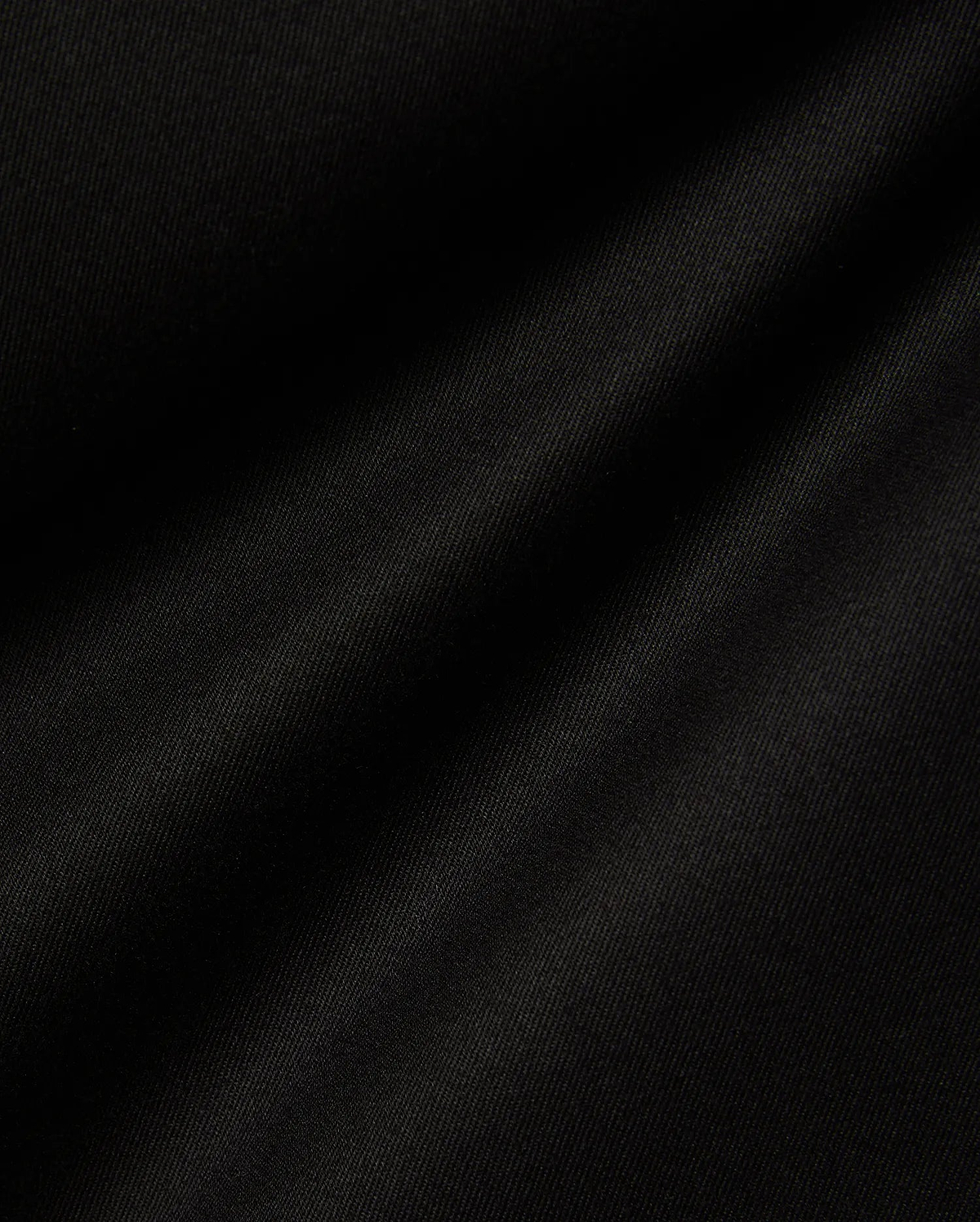 Mens Aidan Chino Pant in deep black, featuring a finely woven twill fabric with distinct diagonal ridges, creating a smooth texture and soft, undulating folds that suggest a comfortable drape. (6)
