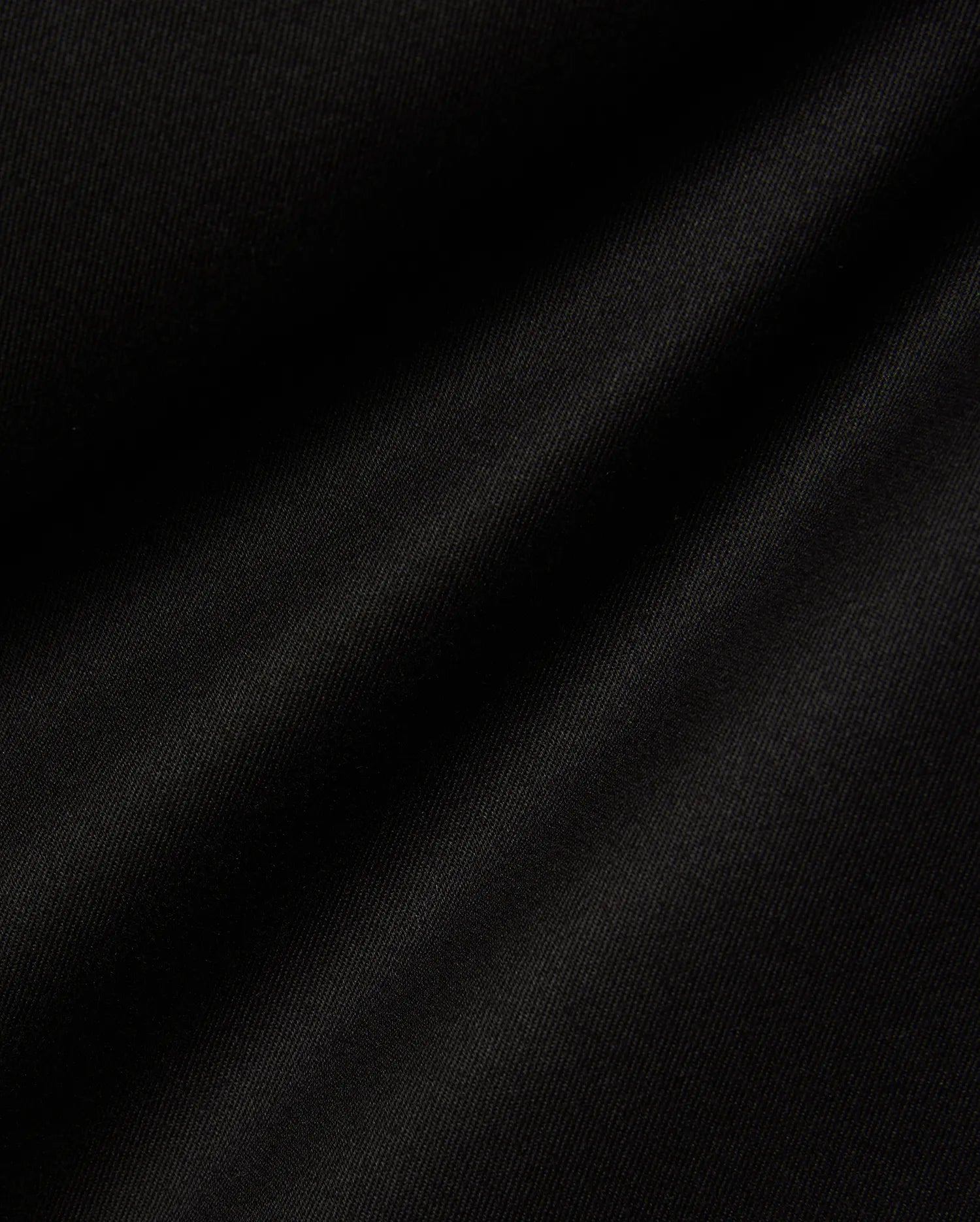 Mens Aidan Chino Pant in deep black, featuring a finely woven twill fabric with distinct diagonal ridges, creating a smooth texture and soft, undulating folds that suggest a comfortable drape. (6)