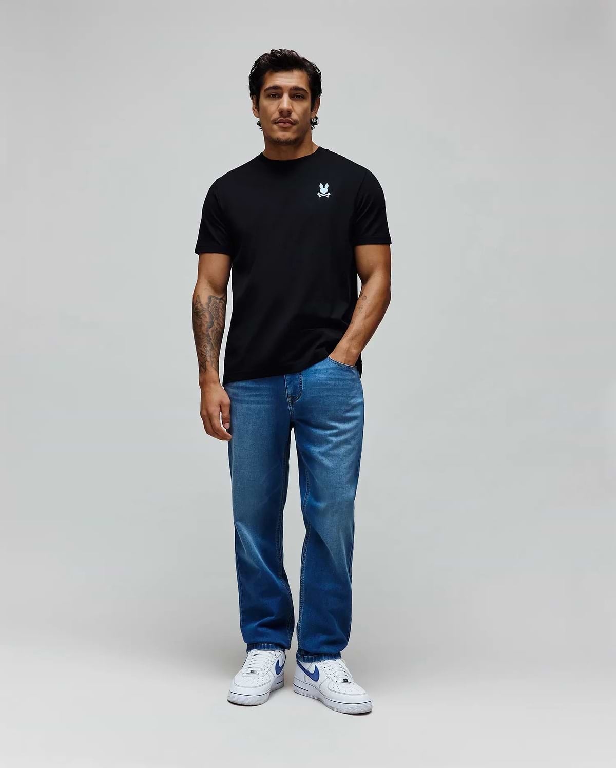 Black classic fit jersey t-shirt with a small embroidered light blue Psycho Bunny skull logo on the left chest, paired with relaxed fit medium blue washed MENS ACE KNIT DENIM PANT.