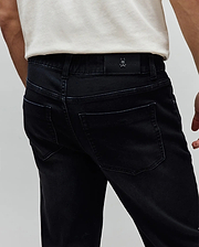 Mens Ace Knit Denim Pant. Washed black classic fit knit denim with back pockets, belt loops, and a small embossed Psycho Bunny skull logo on a black leather patch at the back waistband.