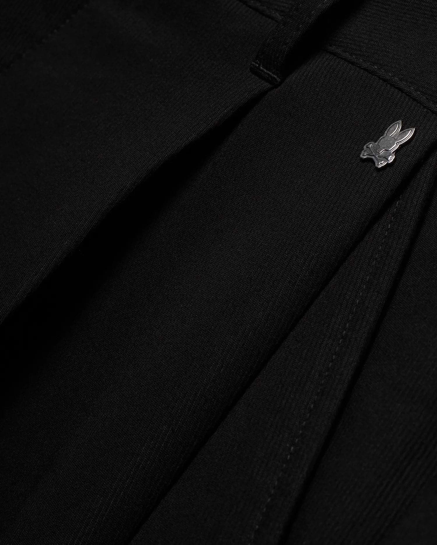Men's Wayde Wide-Leg Pleated Pants in black, featuring a subtle fabric texture, wide-leg fit, and a small metallic silver Psycho Bunny skull logo near the waistband. (6)