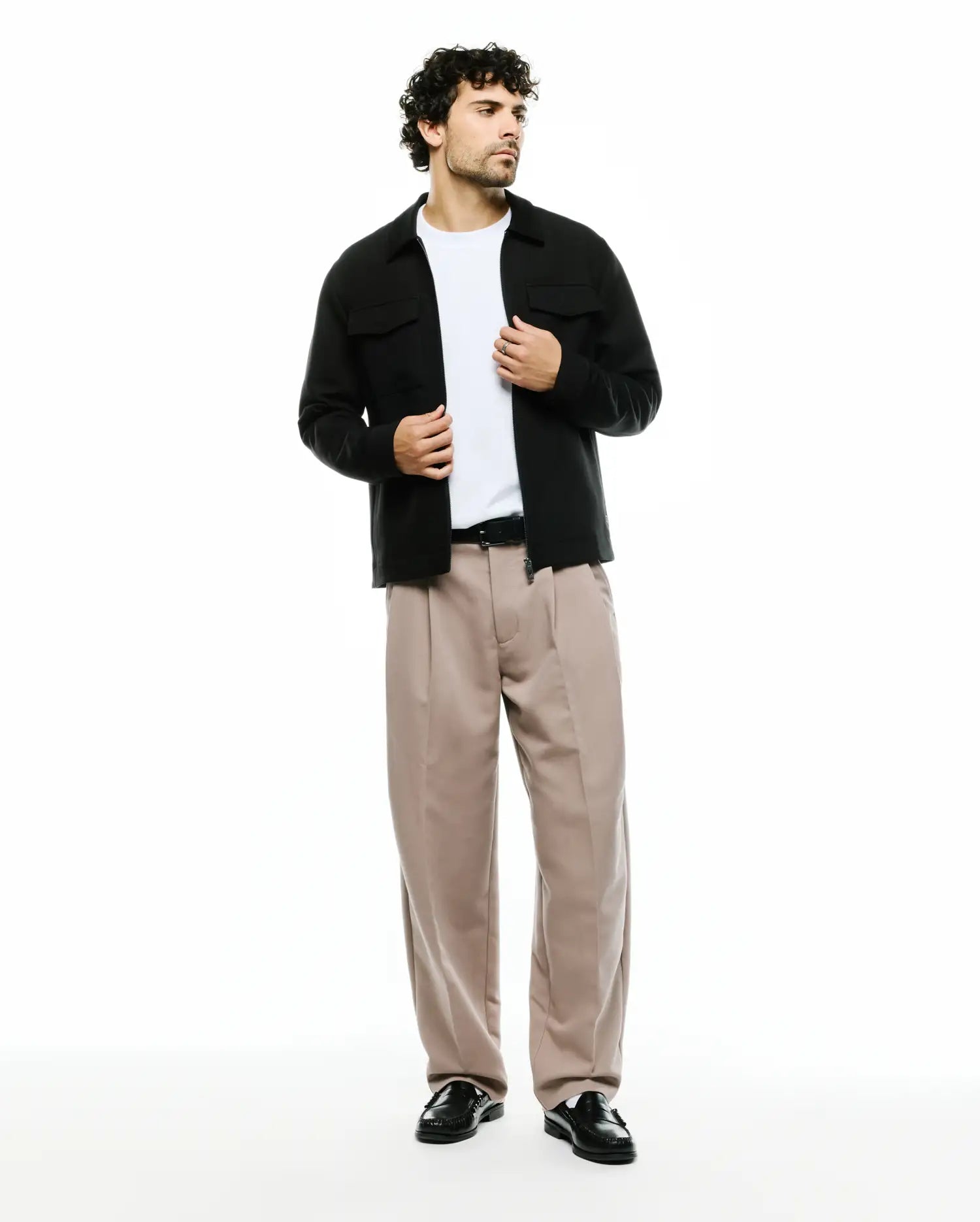 Men's Wayde Wide-Leg Pleated Pants in beige, featuring a relaxed fit and smooth fabric, styled with a black overshirt with chest pockets and a white t-shirt. No visible Psycho Bunny logo. (1)